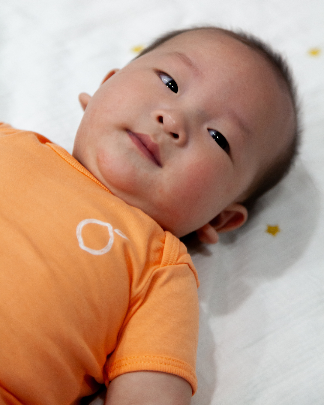 Baby wearing Limau's short sleeve bodysuit in Salmon colour. Its unisex colour is suitable for both baby boy and girl.